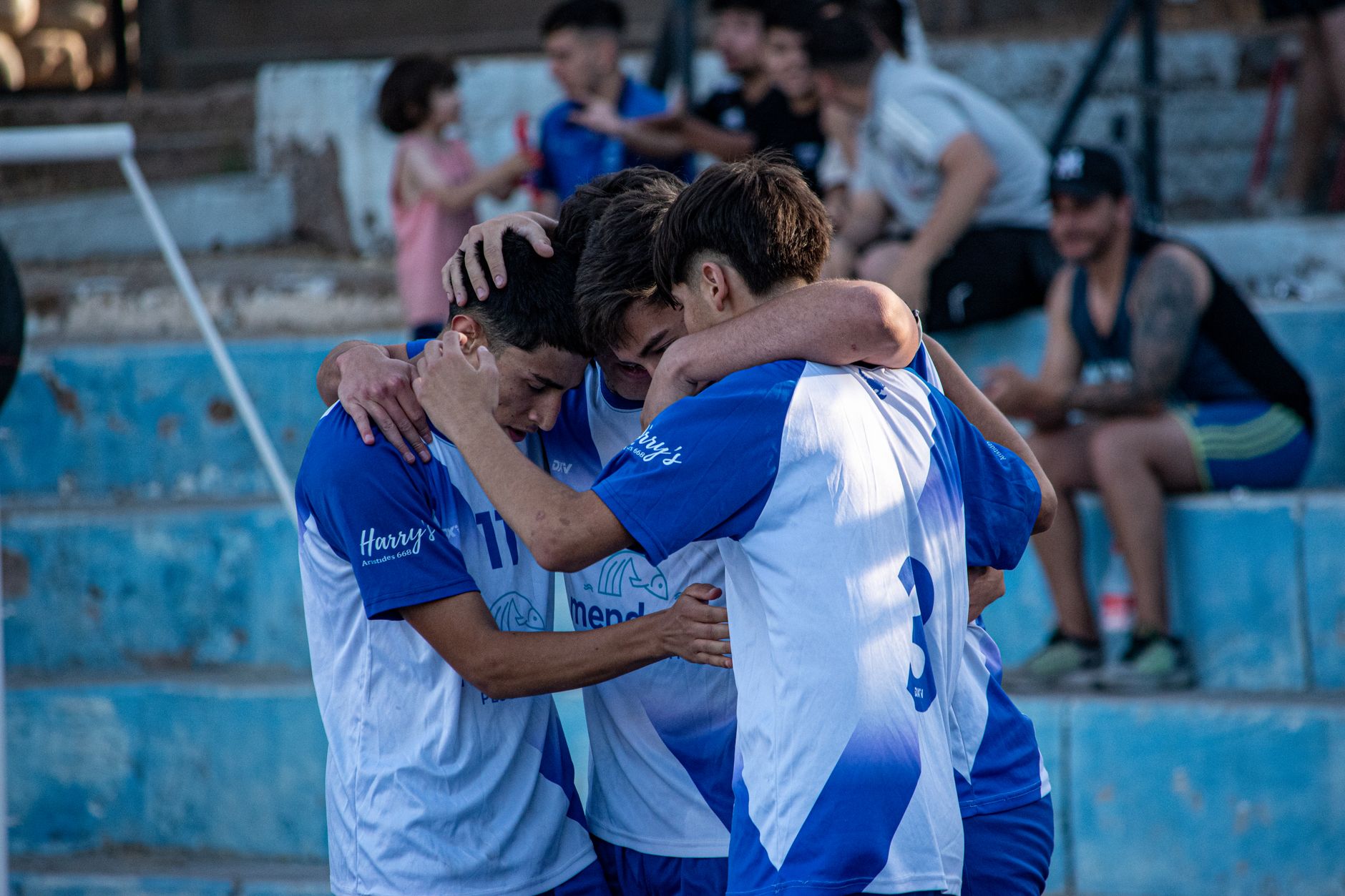 A group of young soccer players share an emotional hug on the field during an outdoor game.