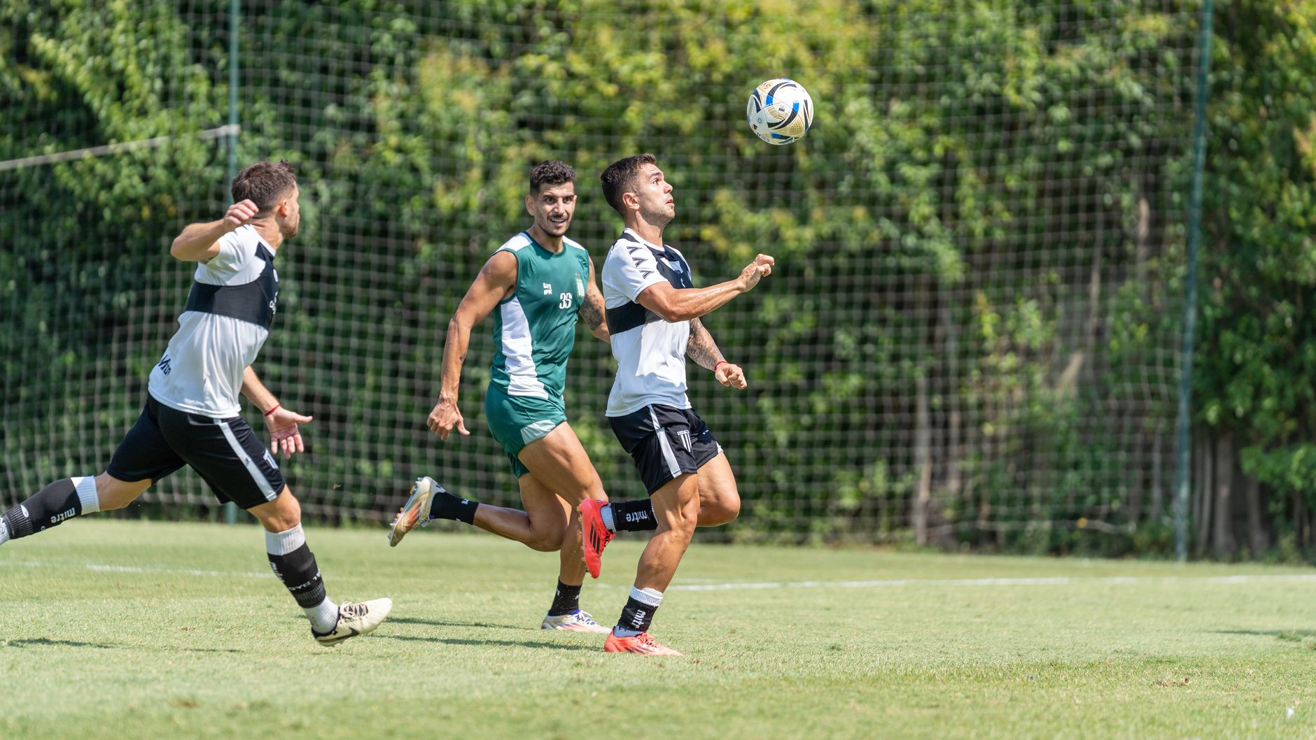Intense soccer game moment with players chasing the ball on a sunny day.