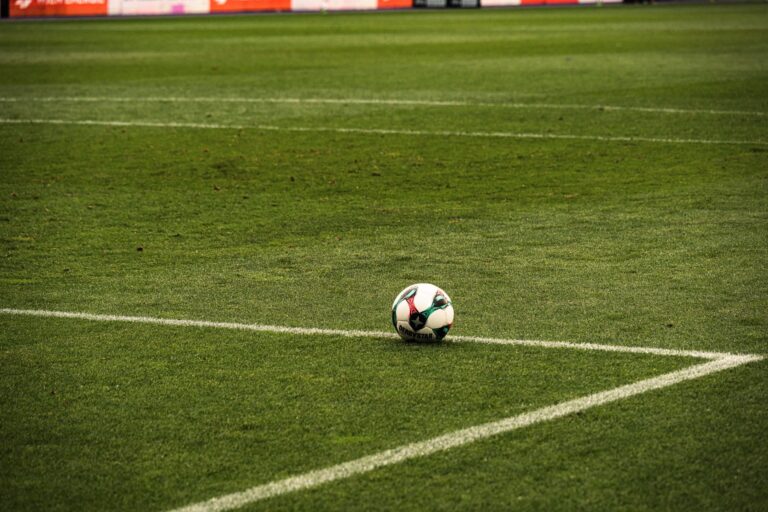 A soccer ball rests on a well-maintained green football field corner, ready for play.