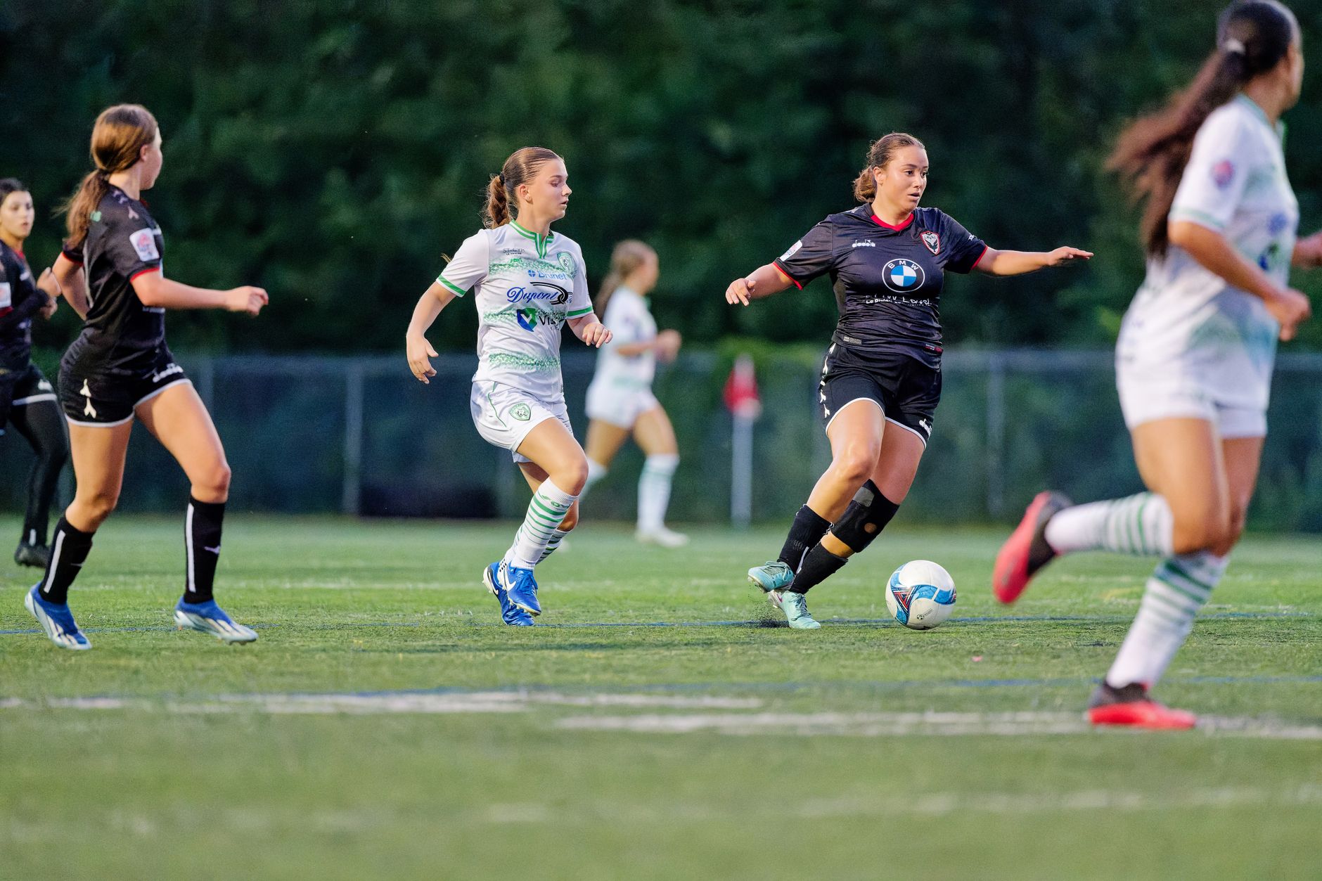 Dynamic action shot of female soccer players in motion during a game on a grass field.