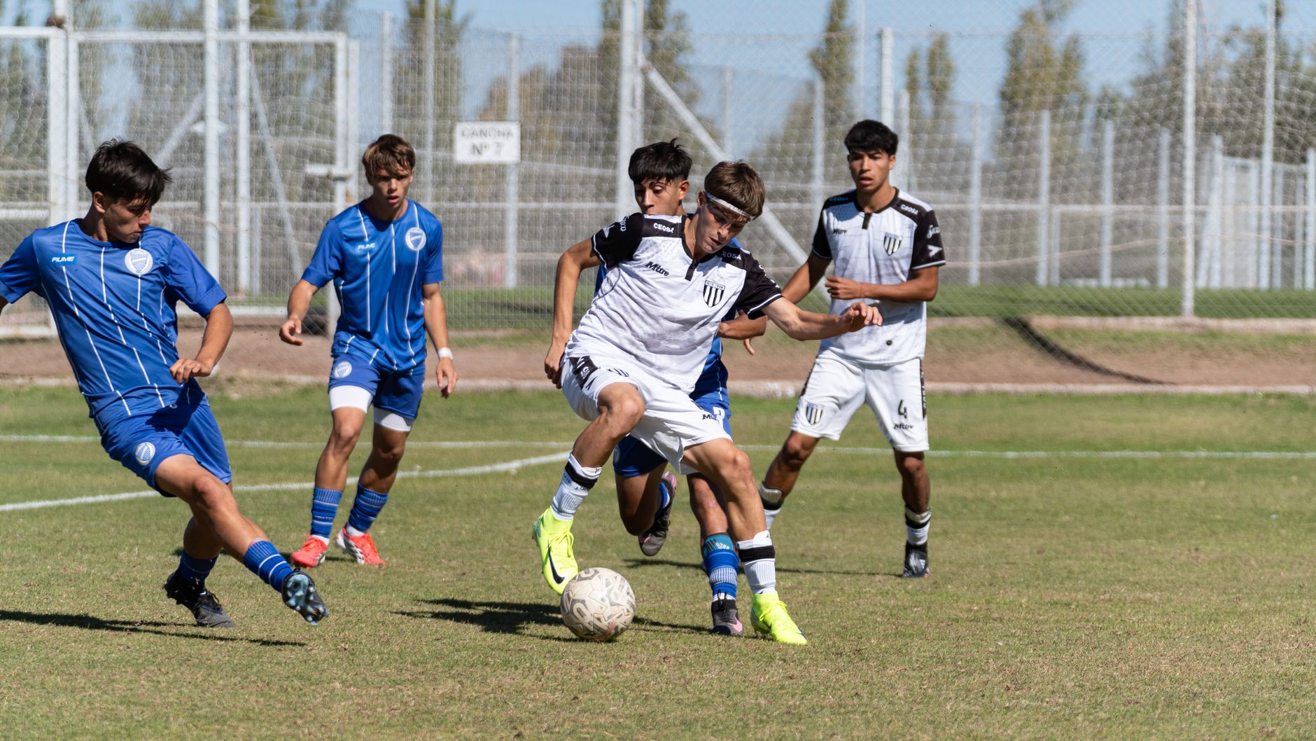 Intense action moment during a youth soccer match with players in blue and white uniforms.