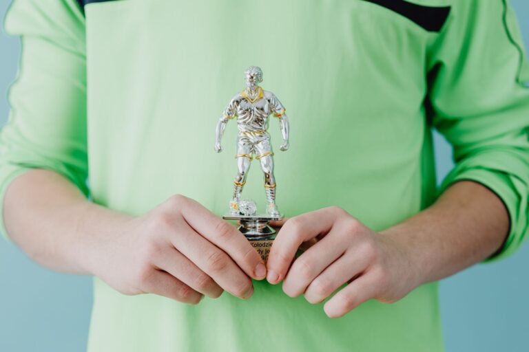 A person holding a silver soccer trophy against a blue background.