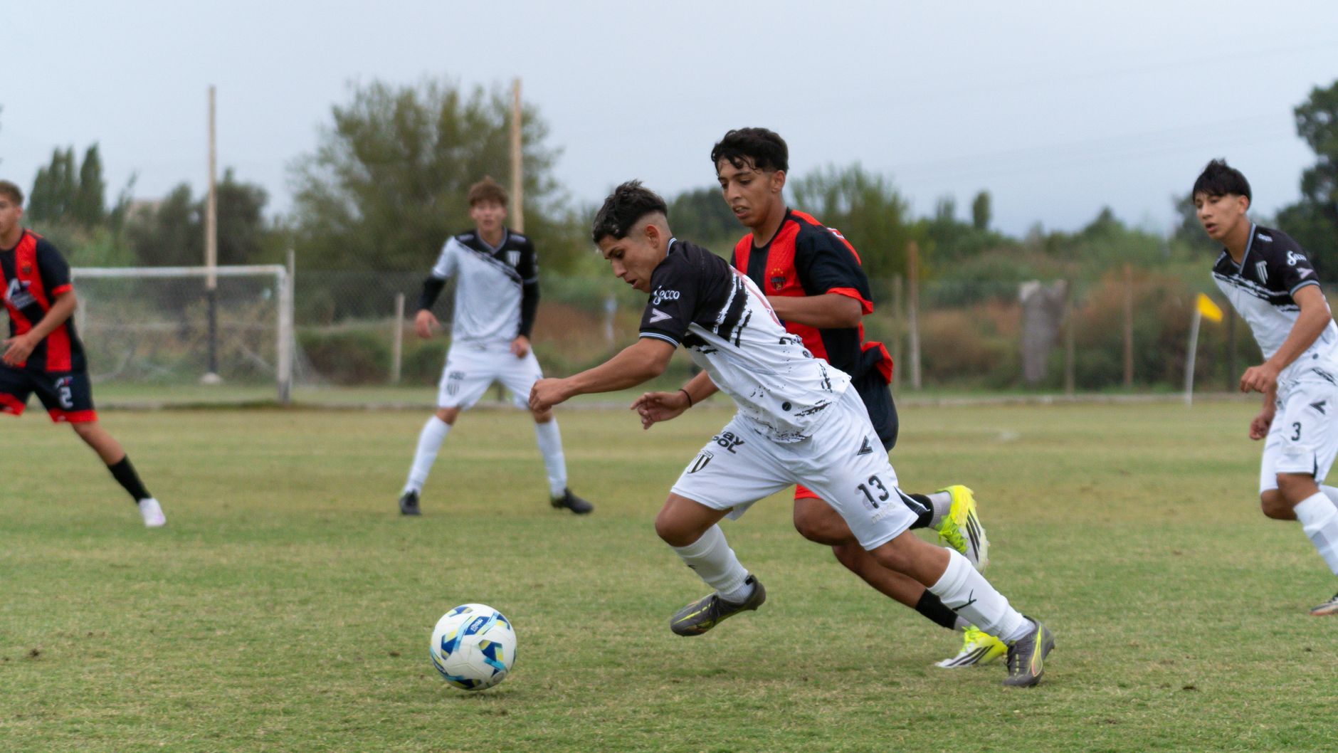 Young athletes in a competitive soccer match, showcasing agility and teamwork on a grassy field under a cloudy sky.