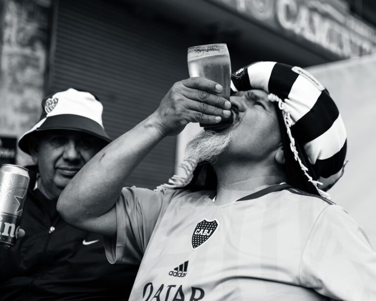 A passionate football fan in a striped hat enjoying a beer on a sunny day with friends.