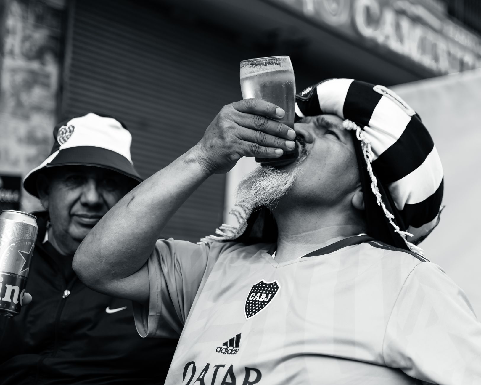A passionate football fan in a striped hat enjoying a beer on a sunny day with friends.