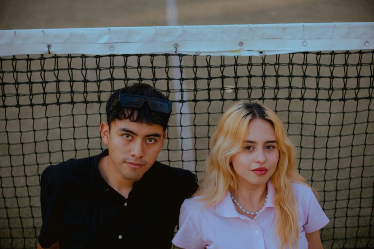 Casual portrait of a young man and woman standing together by a tennis net, creating a relaxed and modern vibe.