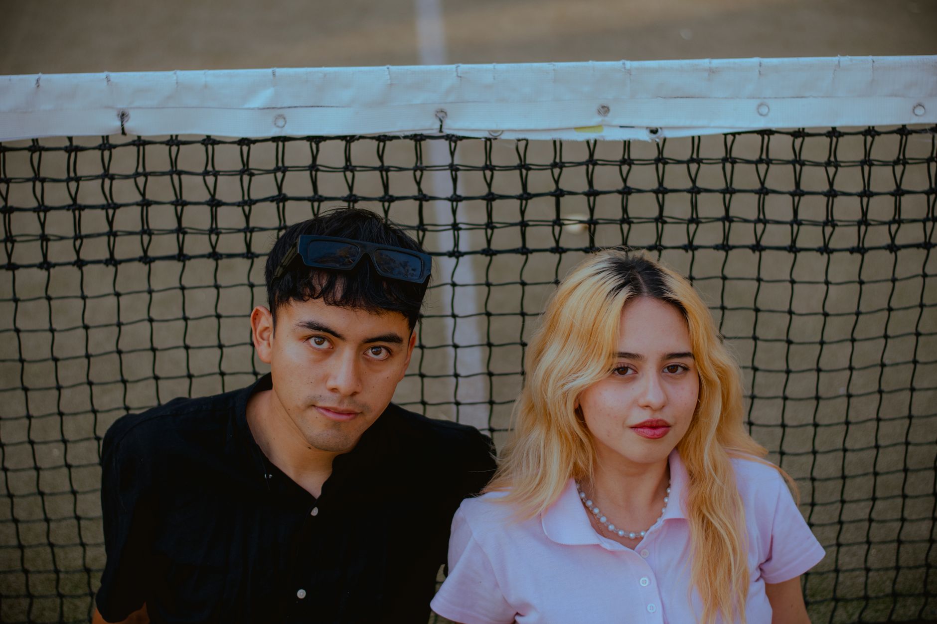 Casual portrait of a young man and woman standing together by a tennis net, creating a relaxed and modern vibe.