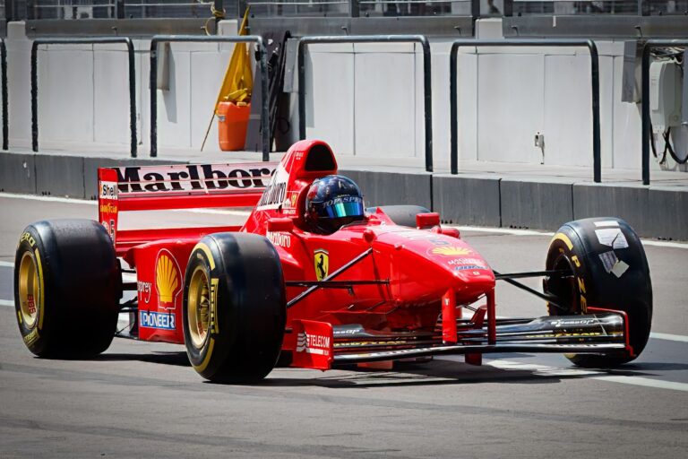 A bright red Formula 1 racing car on a track pit stop area during the day.
