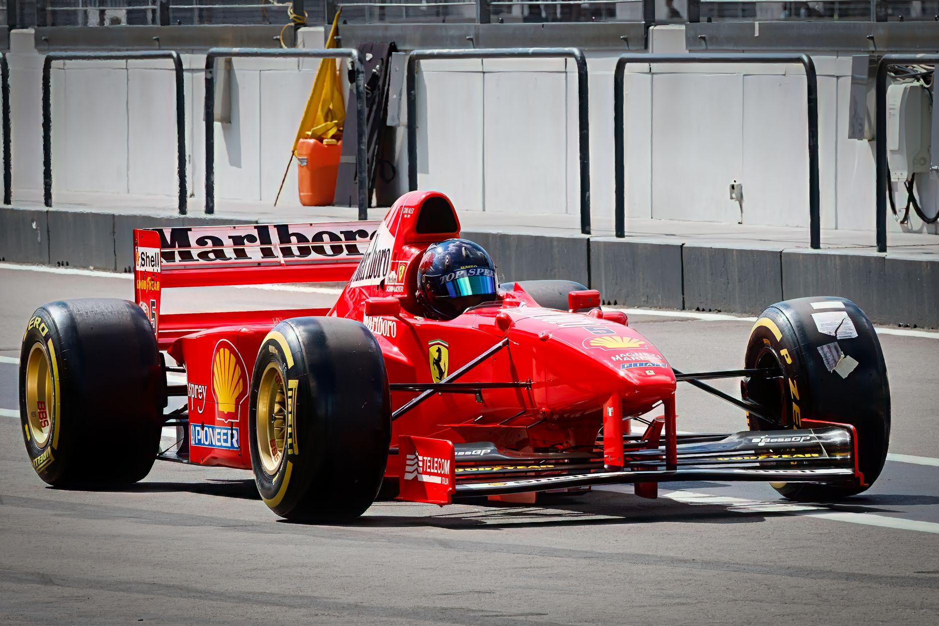 A bright red Formula 1 racing car on a track pit stop area during the day.
