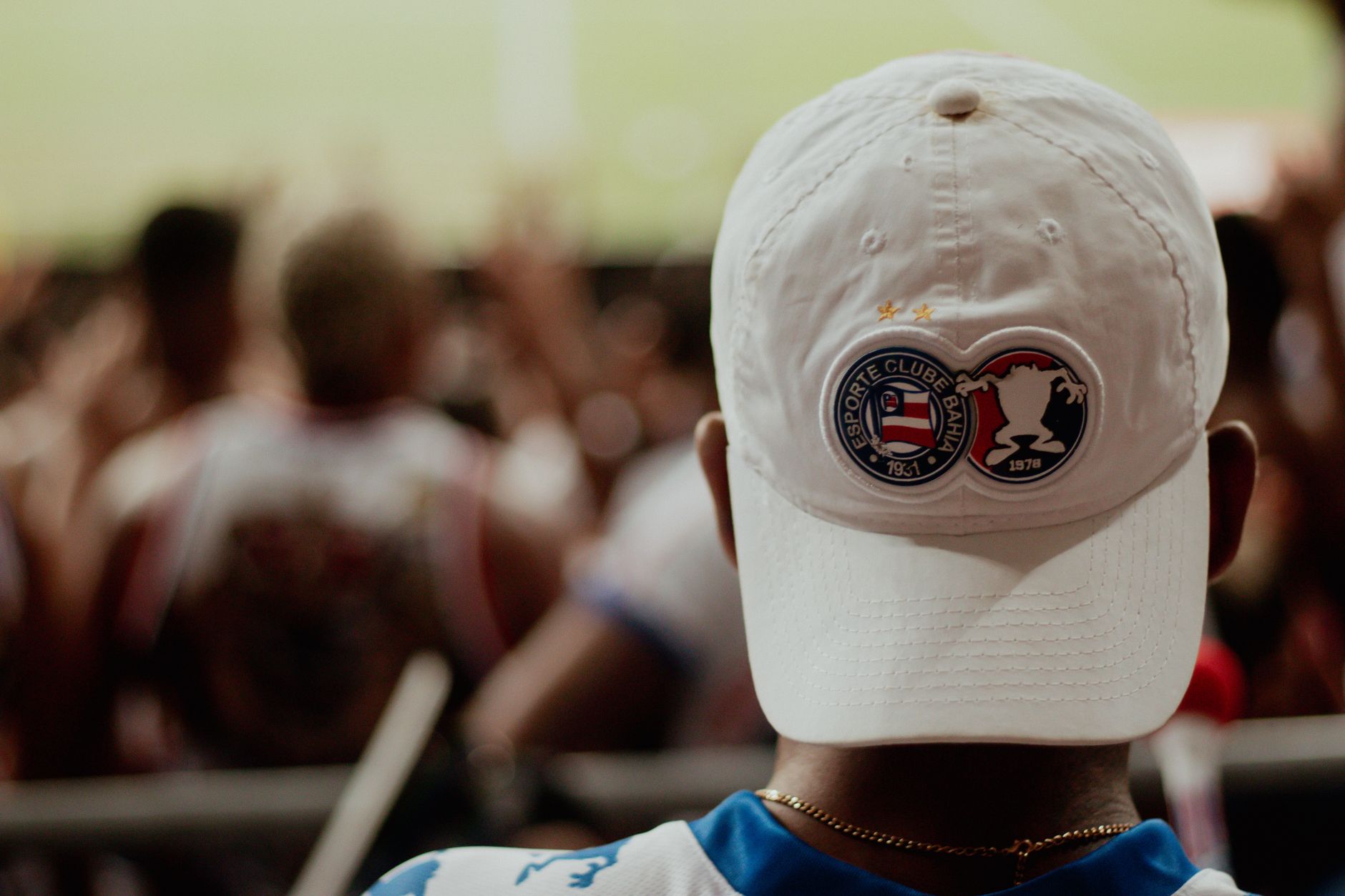 A dedicated football fan sport ing an Esporte Clube Bahia cap watches the game.