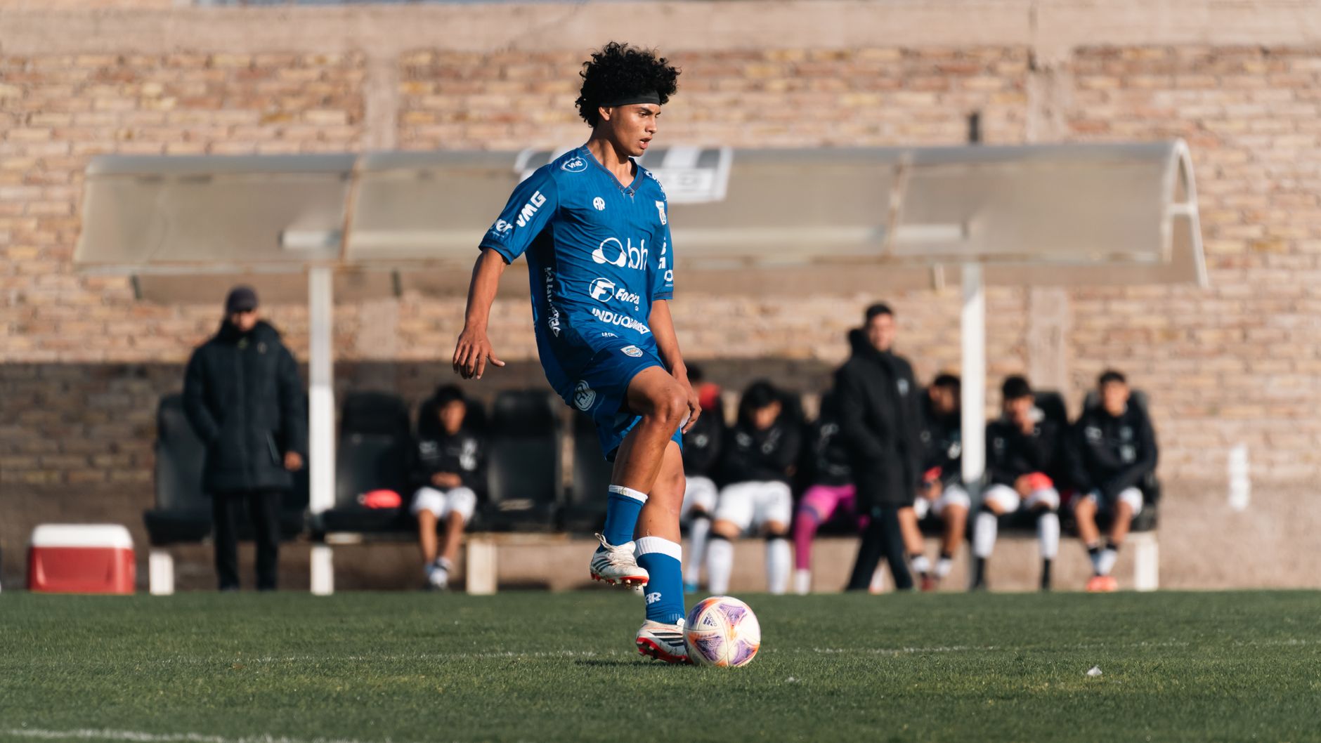 Young soccer player wearing blue uniform playing on a sunny day.