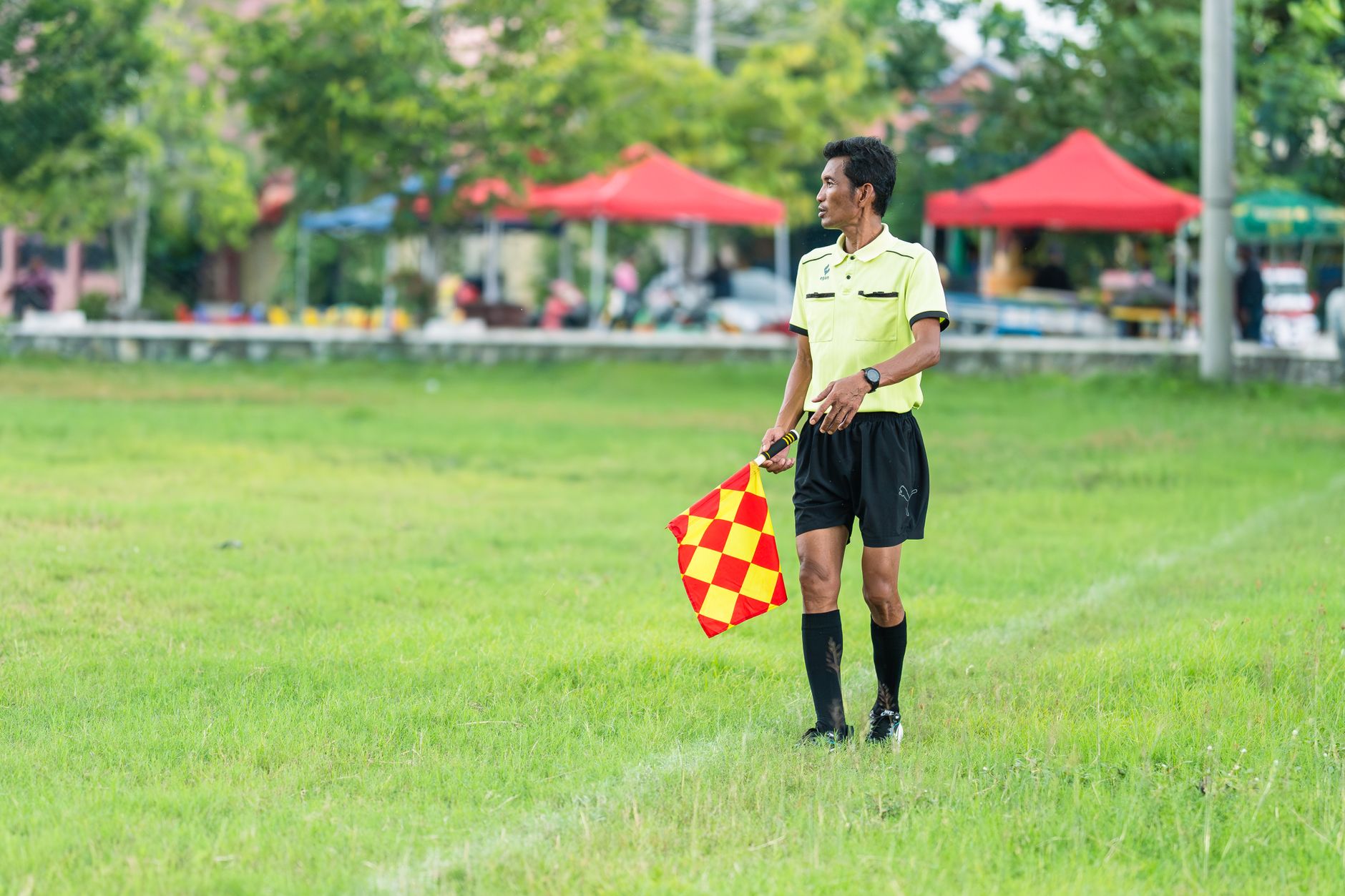A soccer linesman in uniform standing on the grassy field with a flag during a daytime match.