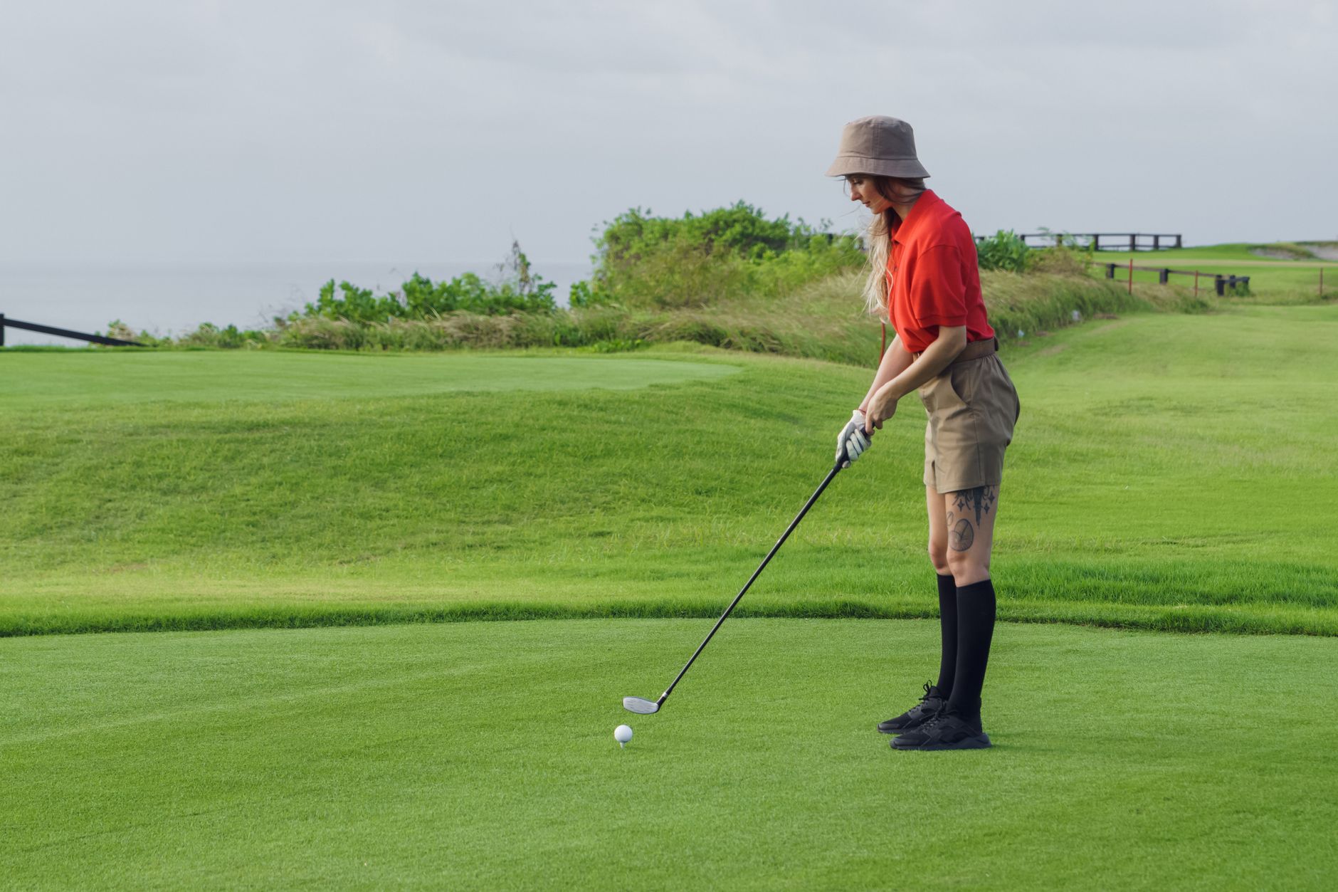 A woman golfer in red shirt on a lush golf course preparing to swing.