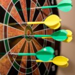 Multiple green and yellow darts precisely hitting a dartboard bullseye, indoor sport scene.