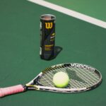 Tennis racket and ball on a bright green court next to a tube of balls.