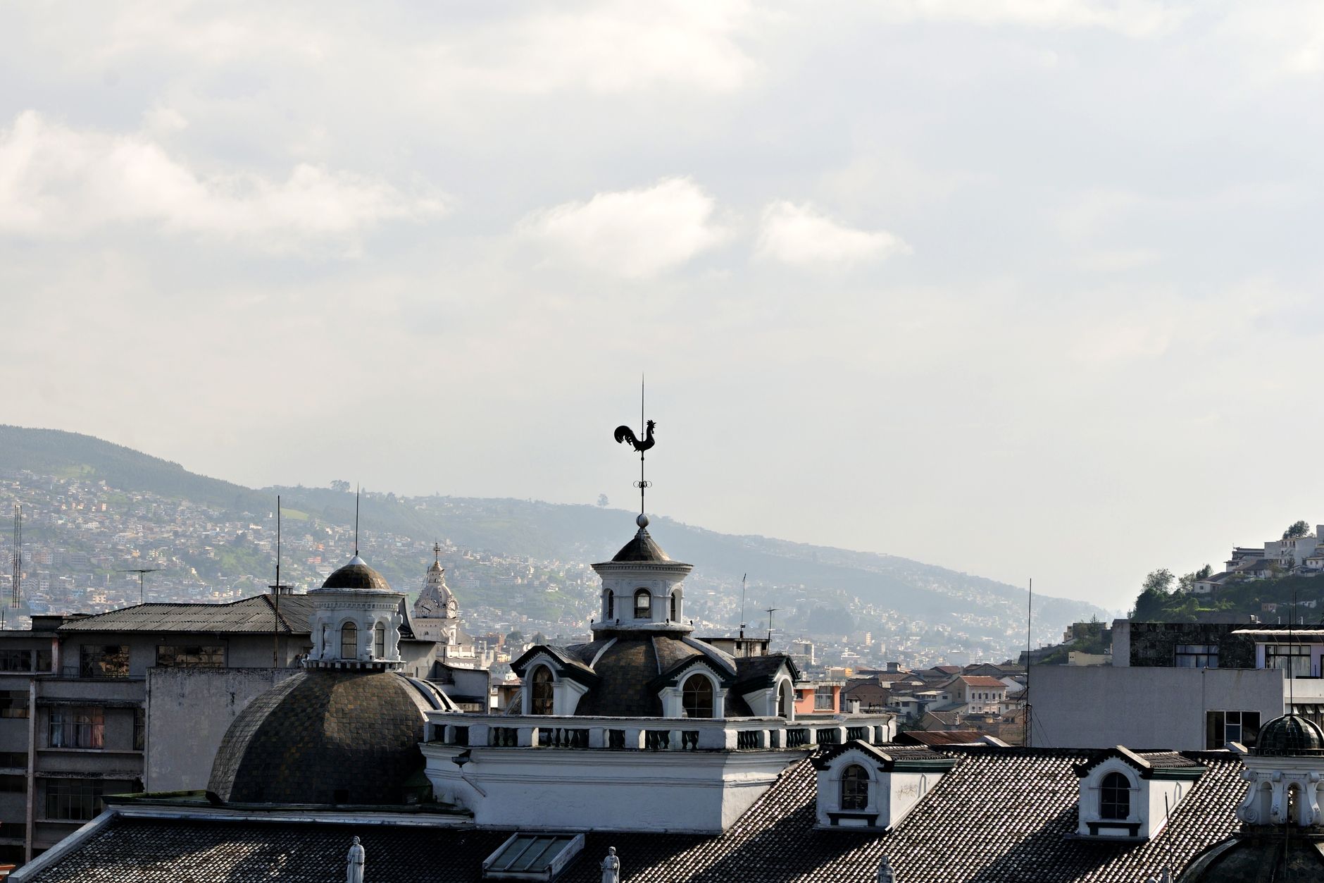 Scenic view of Quito's historic rooftops with Andean mountains in the background under a bright sky.