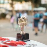 Close-up of a polished soccer trophy with medals at an outdoor sports award ceremony.