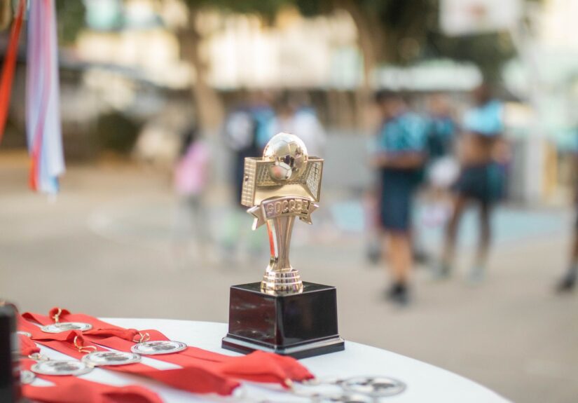 Close-up of a polished soccer trophy with medals at an outdoor sports award ceremony.