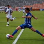 Dynamic soccer match featuring players in blue and white uniforms during a sunny day.