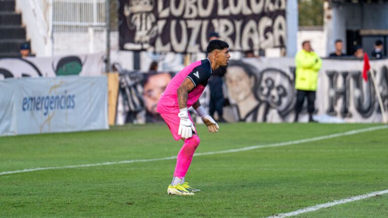 Soccer goalkeeper in vibrant pink uniform poised during a match on a bright day.