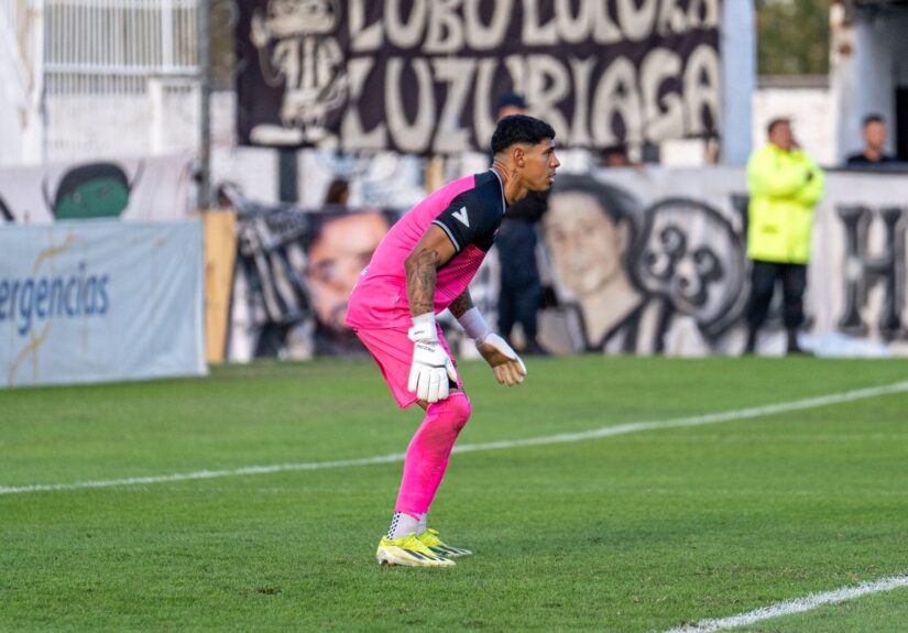 Soccer goalkeeper in vibrant pink uniform poised during a match on a bright day.